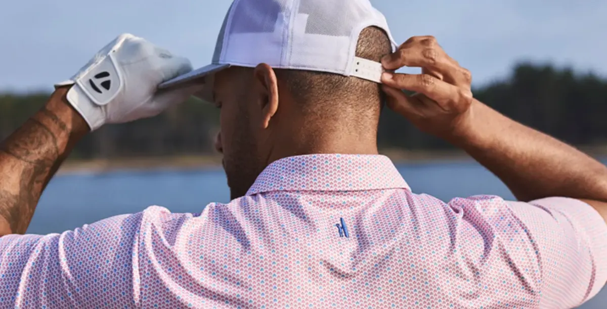 Man adjusting a cap while wearing a pink Johnnie-O polo