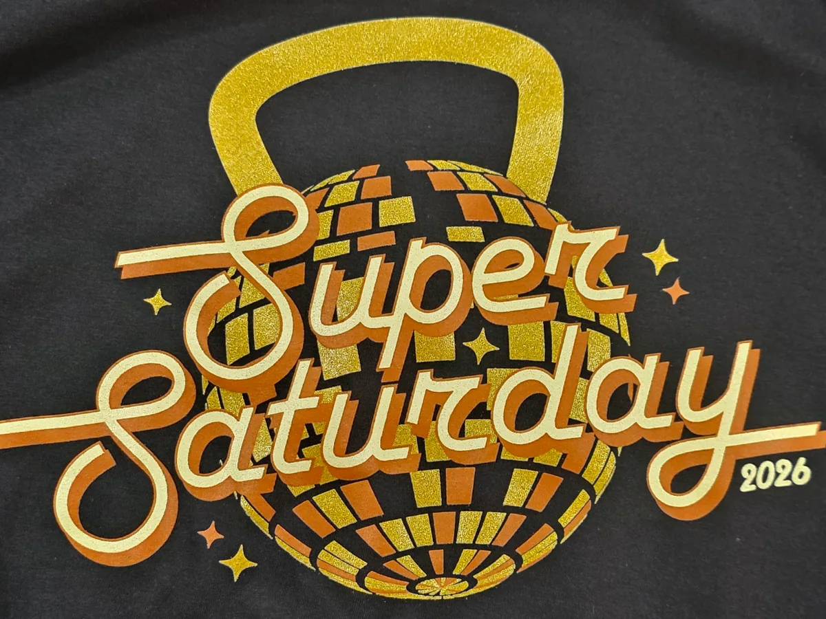 Screen-printed Super Saturday 2026 design in metallic gold and orange inks on a black shirt
